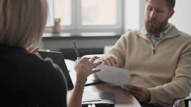 Caucasian colleagues sitting at desk and examining document together while having meeting in office