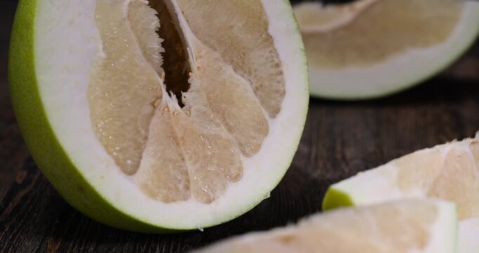 large citrus fruit cut into several pieces with juicy sweet flesh, large citrus fruit cut in half on an old wooden kitchen table, the grapefruit