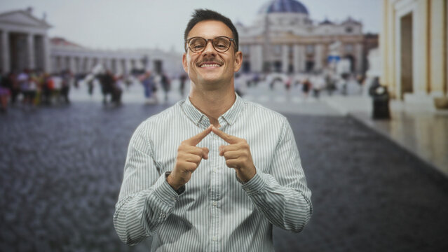 Hispanic man with mustache and glasses, hands clasped with fingers touching, smiling with closed eyes in building with cathedral dome visible; contentment.