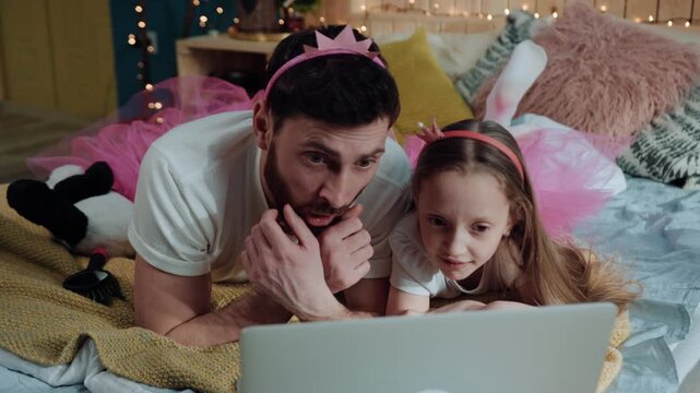 High angle view handsome man father and his daughter watching movies on laptop amaze from the scene with eyes wide-opene. Portrait of dad and young girl showing suprise while looking on screen.