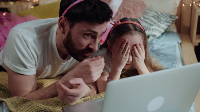 portrait of young man and girl fairies watching scary videos on laptop computer closing their faces lying on bed in girly bedroom at home.