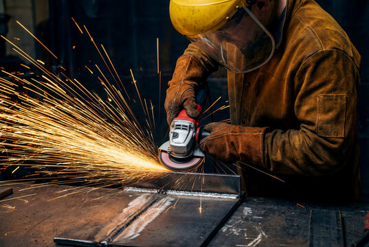 Metalworker Grinding Steel with Angle Grinder and Sparks in Industrial Workshop