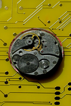 Old mechanical time piece on yellow circuit board illustrating mechanical vs electronic