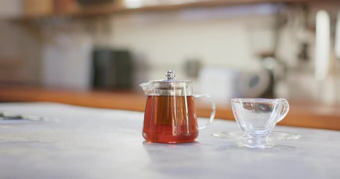 Camera is racking focus and glass teapot is shifting and reflecting on kitchen counter with teacup