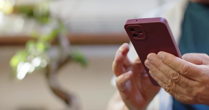 Senior Asian man tapping purple case phone at home adjusting grip, watch bonsai left, copy space