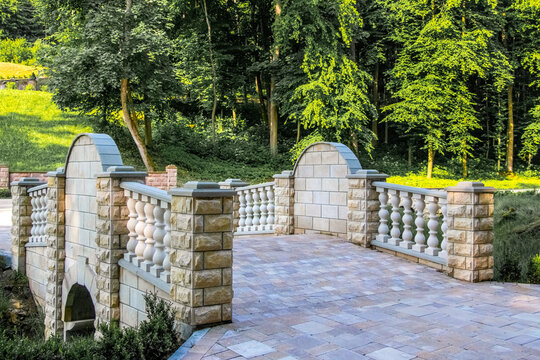 Decorative stone bridge with shaped balusters in a picturesque park against a dense green forest on a sunny day