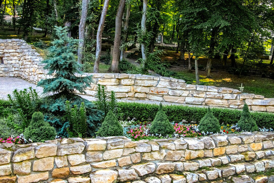 Terraced stone park with decorative conifer trees flower beds and forest path on hillside