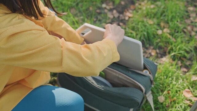 White woman unpacking camping backpack outdoors, hands sorting gear in grass, zipper opening pockets, organizing supplies into compartments, calm focused prep for picnic or hike in sunlit meadow