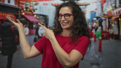 Fototapeta premium Woman wearing red glasses pointing finger at empty space on busy city street under daylight; curiosity.