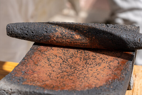 Close-up of a dark volcanic stone metate covered in finely ground red spices under bright daylight.