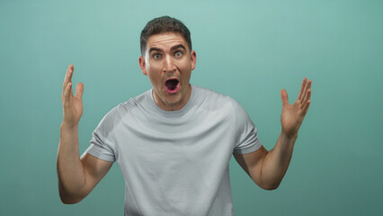 Naklejka premium Young man covering eyes with hands in studio against mint green wall wearing gray tshirt; introspection privacy.