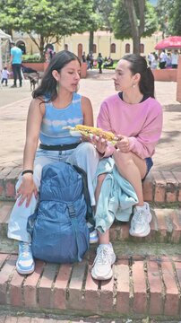 Tourists friends talking and enjoying charred grilled corn on the cob outdoors.