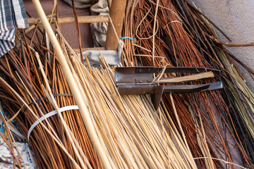A close-up of a metal willow splitter tool resting on bundles of raw and peeled wicker branches. © Sergej