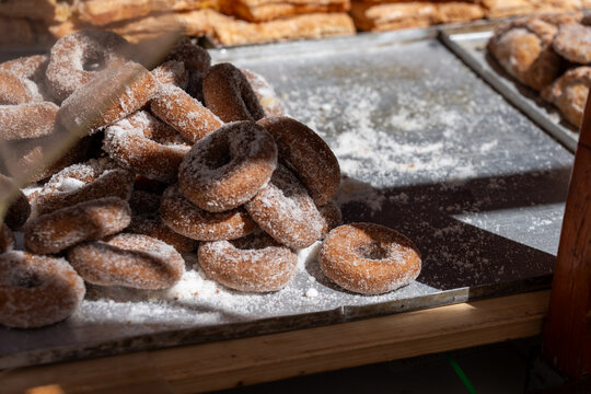 A medium shot of a pile of sugar-dusted doughnuts on a tray, with other pastries visible in the blurred background.
