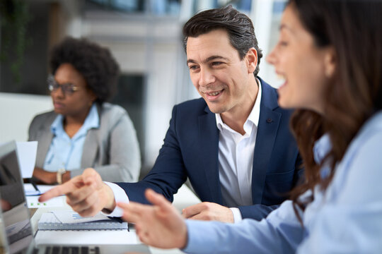 Happy businessman talking to his female colleague while using laptop in the office