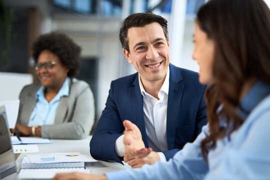 Happy businessman talking to his female colleague while using laptop in the office