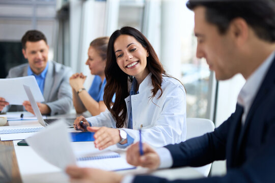 Young female doctor cooperating with an entrepreneur while going through paperwork during a meeting with their colleagues in the office.