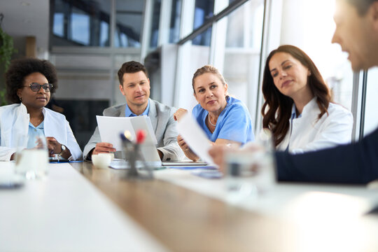 Team of doctors and two businessmen going through paperwork in a hospital.