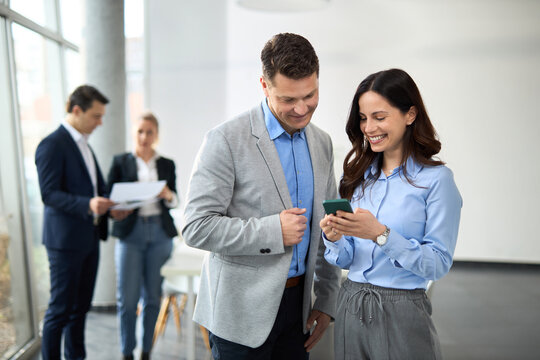 Happy business colleagues using mobile phone in a hallway.