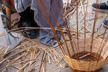 A close-up shot of a half-finished handmade wicker basket with upright willow spokes on a workshop floor. © Sergej