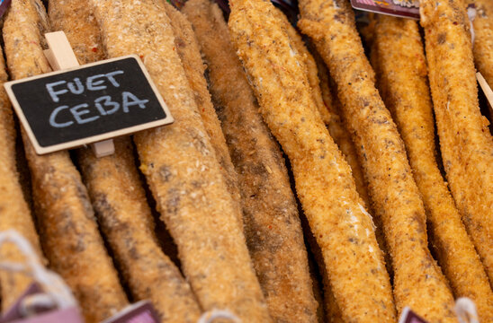 Close-up of Spanish "Fuet Ceba" sausages coated in a golden onion crust with a handwritten chalkboard label.