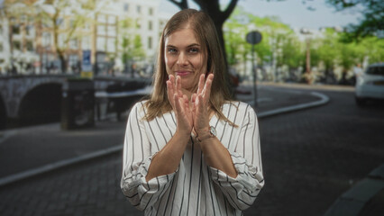 Fototapeta premium Young blonde woman wearing striped blouse clapping hands on street in front of building; celebration joy.