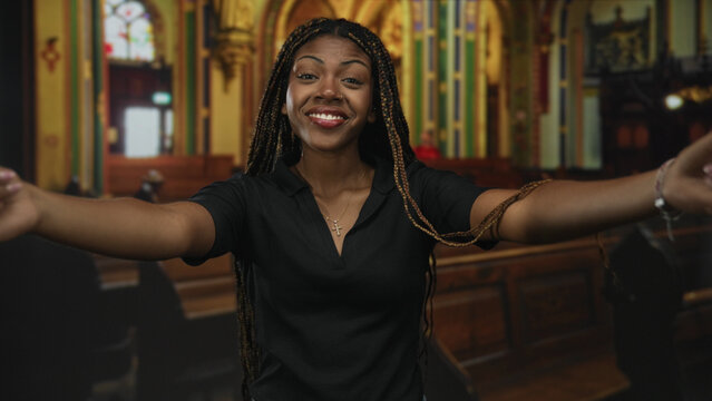 Woman with cross necklace and arms outstretched in church nave, smiling and reaching forward; joy faith welcome.