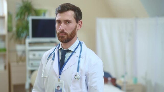 Portrait of competent skillful adult caucasian doctor in white medical gown crossing arms wearing fitness bracelet posing inside hospital room. Healthcare worker. Medical person.