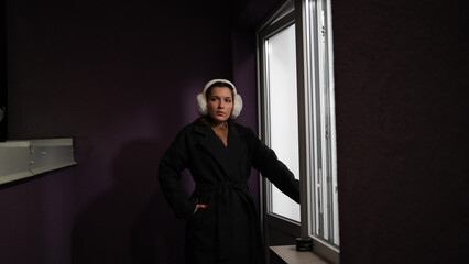 Woman in coat stands on balcony near window in evening city light. © Vasyl