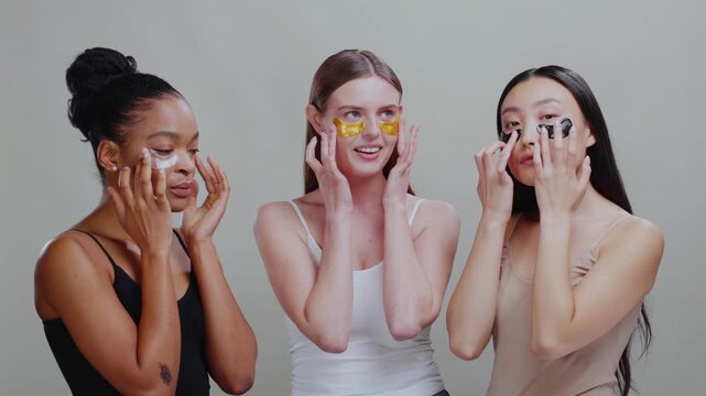 Group portrait of nice pretty multi-cultural women posing at camera applying healthy eye patches for fresh skin. Skincare models. Isolated on background.