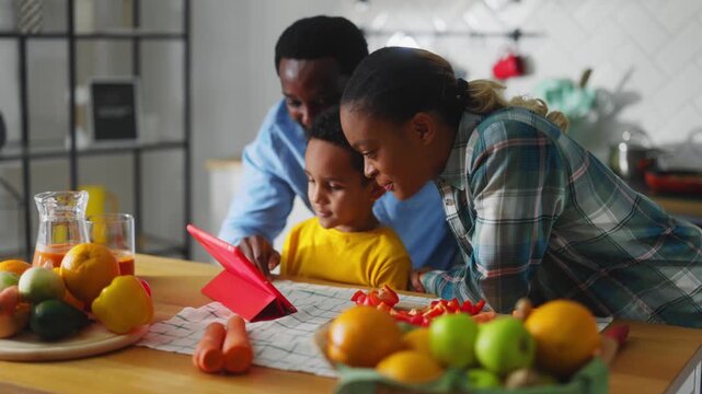Happy attractive afro-american family videochatting with grandparent on tablet computer hugging their son talking online together. Cooking process. technology.