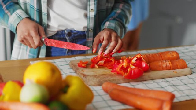 Close-up of young african woman cutting orange carrots for fresh spring salad enjoying cooking with family in home kitchen stylish interior.