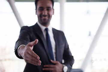 Fototapeta premium Middle Eastern businessman in suit offering a handshake in a modern open-plan corporate office during a meeting