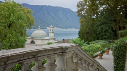 Fototapeta premium Ornate stone terrace balustrade in sharp foreground with shallow defocused lakeside view, domed pavilion and tree lined slope, garden; background backdrop copyspace calm.