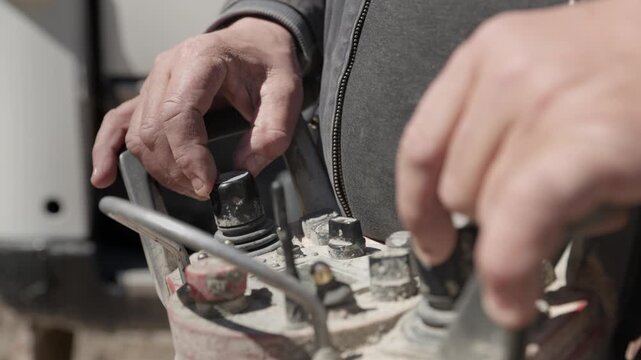 Close up of a machine operator's weathered hands using a dusty industrial remote control with joysticks and buttons, maneuvering heavy equipment at a construction site in bright sunlight