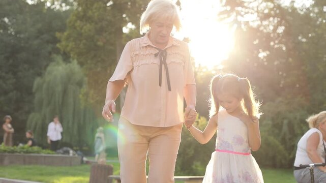 Healthy elderly woman and little lady holding hands and jumping. Beautiful Caucasian grandma and granddaughter having fun together. Outdoors. Summertime