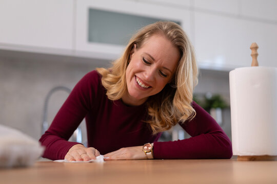 Woman smiling while cleaning kitchen counter with paper towel