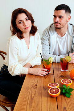 Portrait of young woman sitting with young man, holding citrus drink at cafe table, suggesting casual dating or social meeting. Useful for relationship, lifestyle, hospitality marketing