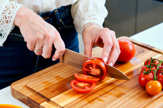Close up of woman hands slicing fresh tomatoes on cutting board, preparing healthy meal ingredients. Suitable for cooking blog, nutrition campaign, recipe content
