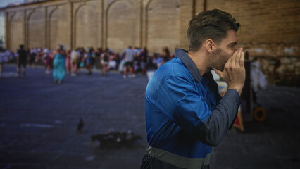 Obraz premium Man bearded worker in blue overalls cupping hands to mouth shouting toward a crowd on street by stone wall; crowd attention urgency.