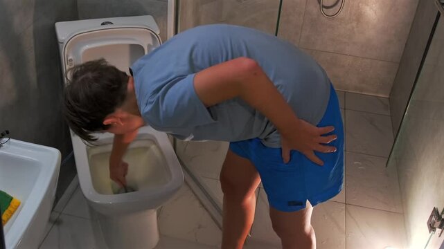 Woman feeling unwell leans over toilet in bathroom, experiencing nausea and sickness. Concept of food poisoning, illness, stomach pain and health problem in everyday home situation