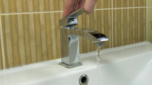 Close-up of a person turning on a bathroom faucet, which starts to flow with running water, then turning it off