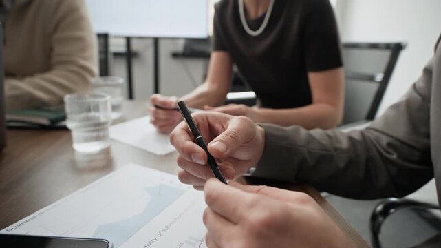 Close up shot of anonymous man holding pen while sitting at desk during offline meeting in office