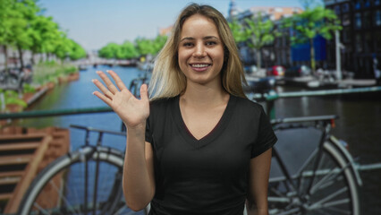 Obraz premium Woman waving hand by bicycle on street in amsterdam, smiling to camera while wearing black t shirt; friendly greeting.