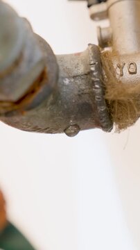 water dripping from metal tap close up for plumbing leak concept with flowing drops and pipe detail