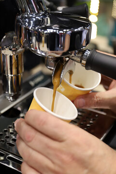 caf&eacute; saliendo de la maquina de expreso de una cafeter&iacute;a cayendo en vasos para servir y las manos del barista sujet&aacute;ndolos