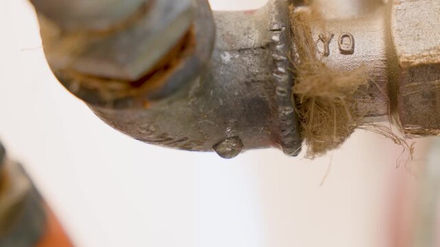 water dripping from metal pipe close up for plumbing leak concept with drop forming and industrial detail