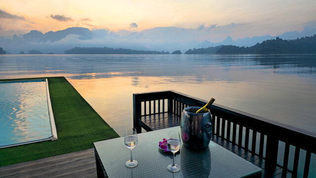 Table with two glasses and bottle overlooking  infinity pool and Cheow Lan Lake at sunset, Khao Sok National Park, Thailand, Southeast Asia.