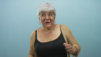 Woman raising arms and smiling with exposed shoulders and hoop earrings against a blue studio backdrop, wearing a cardigan and tanktop  joy celebration. © Krakenimages.com