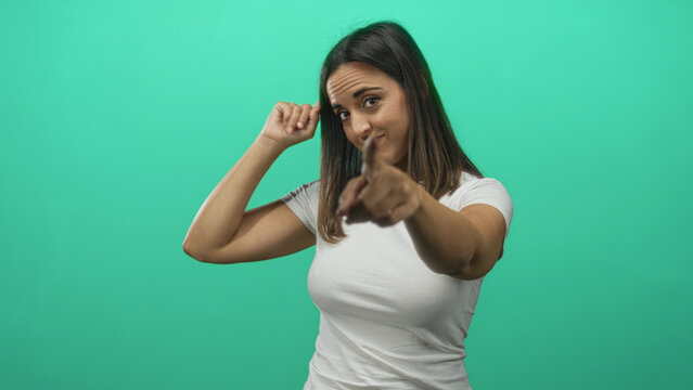 Young woman in white t shirt pointing index finger toward camera while touching her temple with other hand in studio; playful confidence.